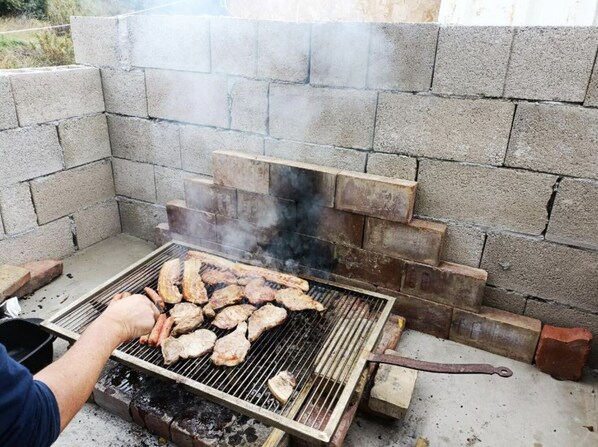 A portable grill with meat being cooked, surrounded by concrete blocks.