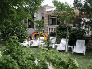 Een tuin met witte lounge stoelen, een opblaasbaar glijbaantje in vrolijke kleuren, en een gebouw met een bord waarop 