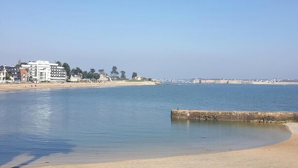 A coastal view with a sandy beach, calm water, and buildings in the background. - Charming farmhouse in the town center and within walking distance of the beaches (Larmor-Plage)