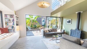 A modern living room with a sofa, a bookshelf, a fireplace, and a large window overlooking a garden. - Elegant Breton farmhouse 5 minutes from the ocean, beaches, and town center (Larmor-Plage)