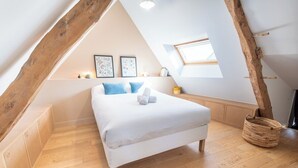 A bedroom with a sloped ceiling, a bed with white bedding, two pillows, a small bedside table, and a window. - Elegant Breton farmhouse 5 minutes from the ocean, beaches, and town center (Larmor-Plage)