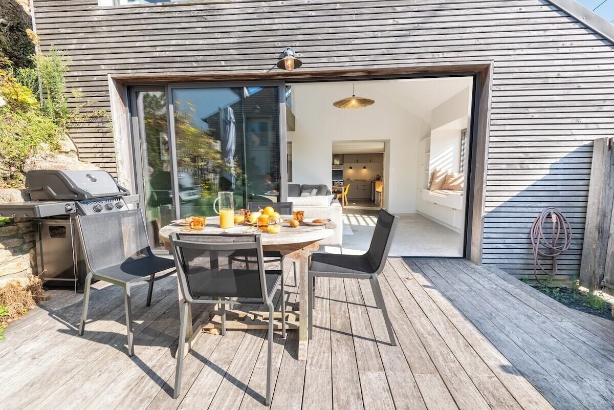 Terraza exterior con mesa redonda y sillas, una parrilla y una puerta de vidrio que da a un interior moderno.
