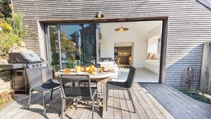 An outdoor deck with a round table and chairs, a grill, and a glass door leading to a modern interior. - Elegant Breton farmhouse 5 minutes from the ocean, beaches, and town center (Larmor-Plage)