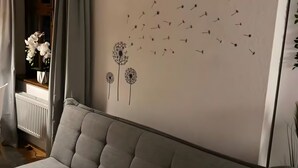 A grey sofa with a cushion, a wall with a dandelion and bird decoration, and a radiator. - Apartment 3 in the Heart of Ulm with Wi-Fi (Ulm)