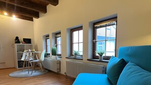 A room with a blue sofa, a white desk with a chair, a radiator, and windows with blinds. - Apartment 6 Ulmer Spatz with Wi-Fi (Ulm)