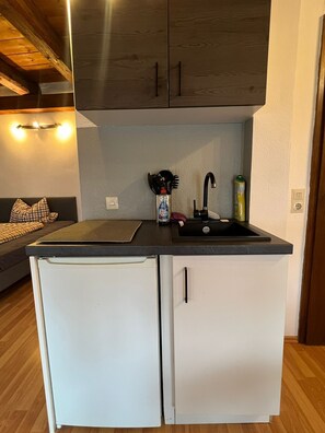 Une cuisine de taille réduite, équipée d’un réfrigérateur, d’un évier et de meubles de rangement en bois.