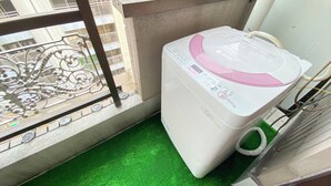 Ein Balkon mit Waschmaschine, Kunstgrasebelag und Metallgeländer.