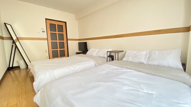 Ein Hotelzimmer mit zwei Betten, einem Fernseher, einem kleinen Tisch und Holzboden.
