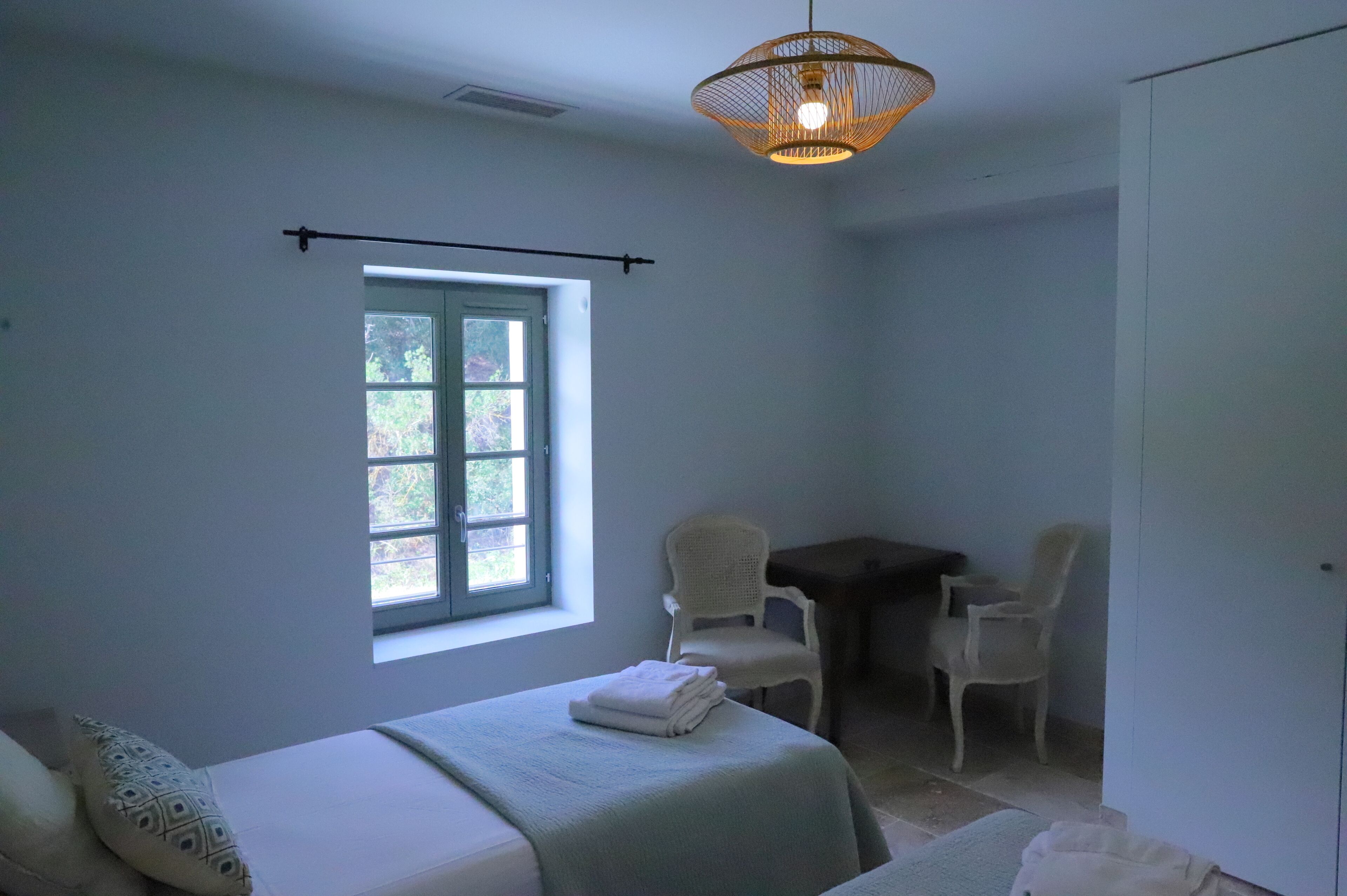 Ein Zimmer mit einem Bett, einem Fenster, einem Schreibtisch, zwei Stühlen und einer Pendelleuchte.