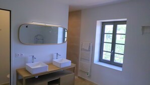Ein Badezimmer mit zwei Waschbecken, einem Spiegel, einem Handtuchhalter und einem Fenster.