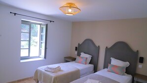 Ein Hotelzimmer mit zwei Betten, einem Fenster mit Vorhängen, einer Deckenlampe und einem kleinen Tisch.
