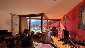 En rummelig opholdsstue med en stor skydedør, der fører ud til en balkon med udsigt til et bjerglandskab.