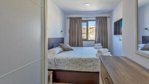 Ein Hotelzimmer mit einem Bett, einer Holzkommode, einem Fenster mit Vorhängen und einem an der Wand befestigten Flachbildfernseher.