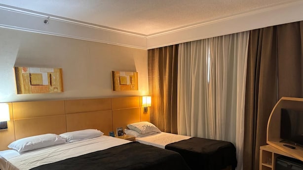 A hotel room with two beds, a TV, and a desk. - Guarulhos Flats Services (Guarulhos)