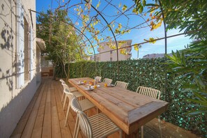 An outdoor wooden deck with a table and chairs, surrounded by greenery and a hedge. - 6 BEDROOM TOWNHOUSE TERRACE A6B002 (Cannes)