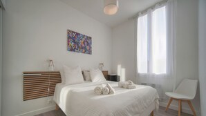 Camera da letto moderna con un letto grande, un comodino, una sedia, un quadro astratto colorato e una finestra con tende leggere.