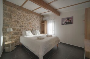 A bedroom with a stone wall, a bed with white linens, a bedside lamp, and a painting on the wall. - 6 BEDROOM TOWNHOUSE TERRACE A6B002 (Cannes)