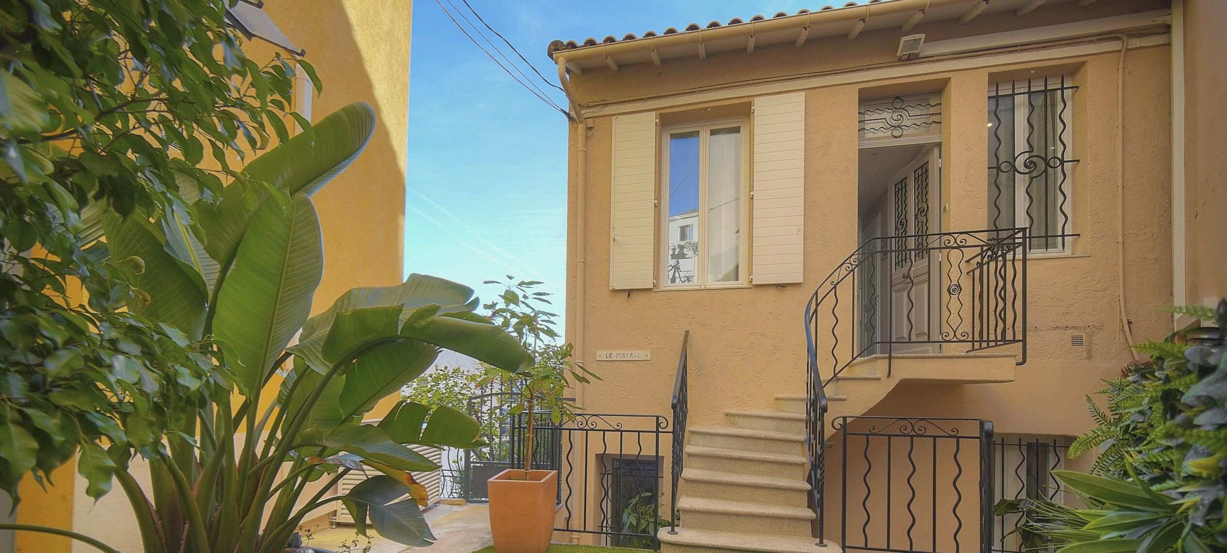 A yellow building with a staircase leading to a balcony, surrounded by greenery.