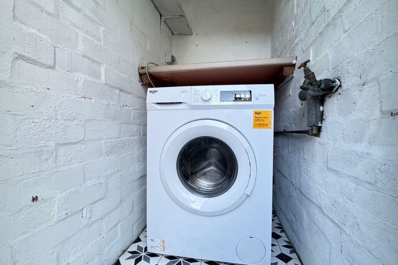 A white washing machine in a narrow space with white brick walls and a tiled floor.