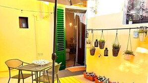 Een gele kamer met een tafel en stoelen, een hangende plantenbak en een groene deur.