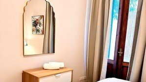 Een hotelkamer met een bed, een houten dressoir, een spiegel en een raam met gordijnen.