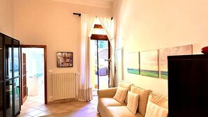 Een ruime woonkamer met een beige bank, een glazen kast en uitzicht door een raam met gordijnen.
