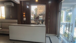 A reception area with a white reception desk, a sofa, and a staircase leading to an upper floor. - R D Palace and Resort (Bakshi Ka Talab)