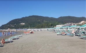 Ein Strand mit mehreren Reihen Sonnenliegen und Sonnenschirmen, einem Rettungsboje und einigen Spaziergängern.