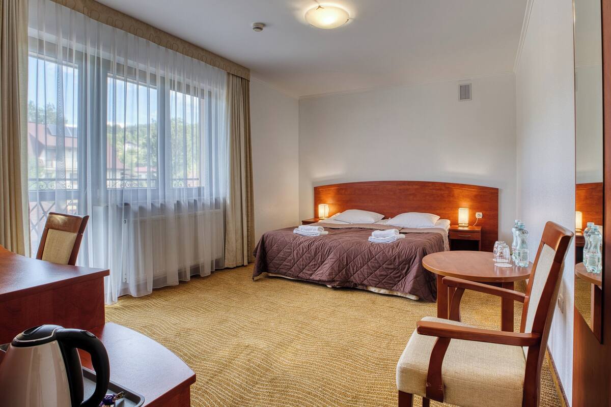 Una camera d'albergo con un letto, una scrivania, una sedia, un tavolo e una finestra con tende.