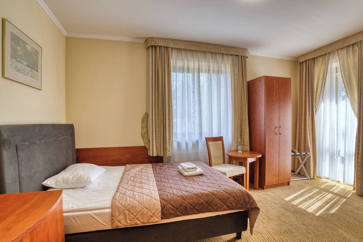 Una camera d'albergo con un letto, un armadio in legno, un tavolino e una sedia.