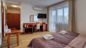 A hotel room with a bed, a desk, a chair, a television, and a window with curtains.