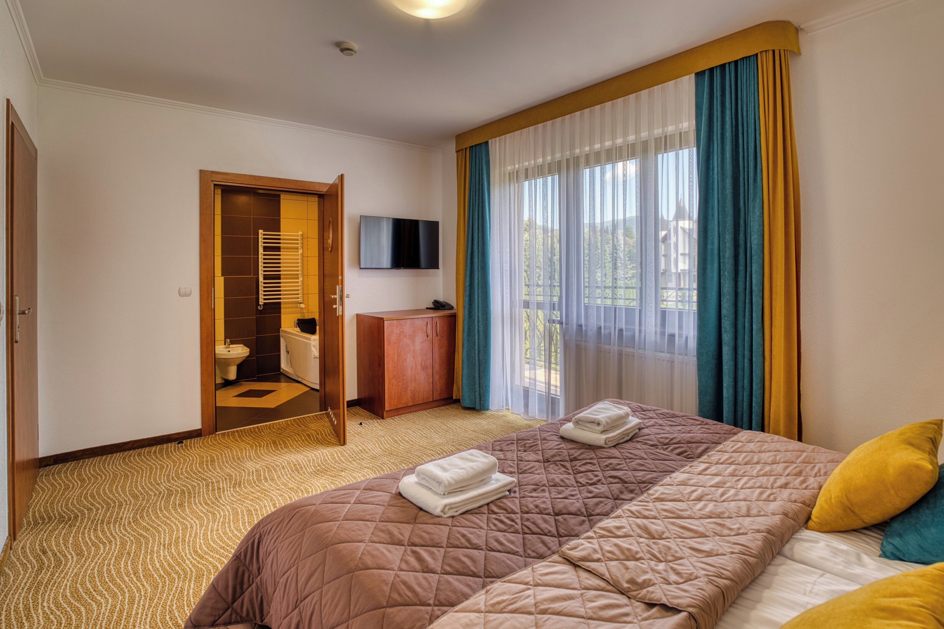 A hotel room with a bed, a desk, a TV, and a bathroom visible through an open door.