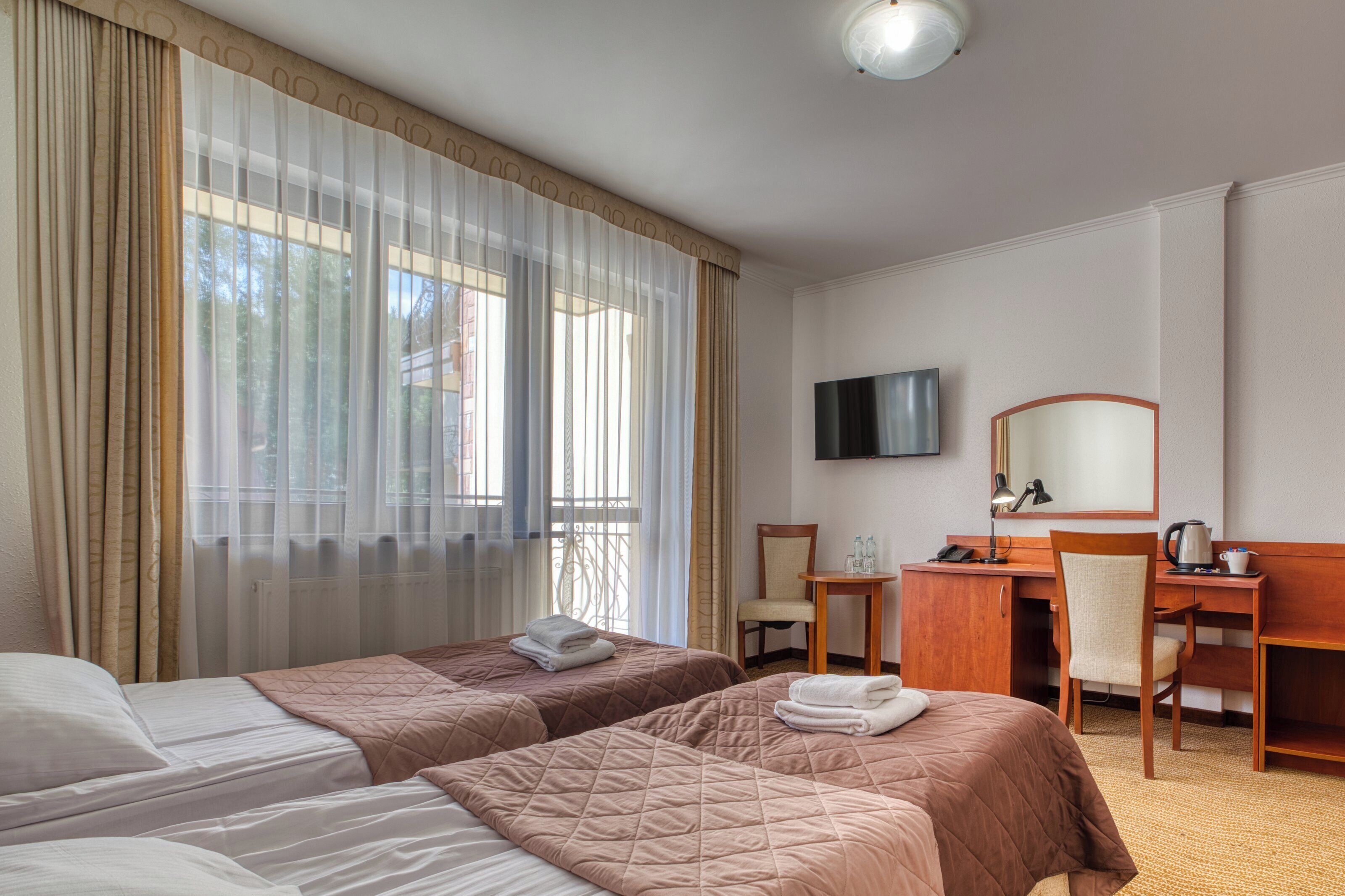 A hotel room with two beds, a desk, a chair, a television, and a window with curtains.