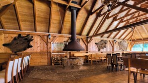 A rustic interior with wooden beams, stone fireplace, and animal skins on the walls.