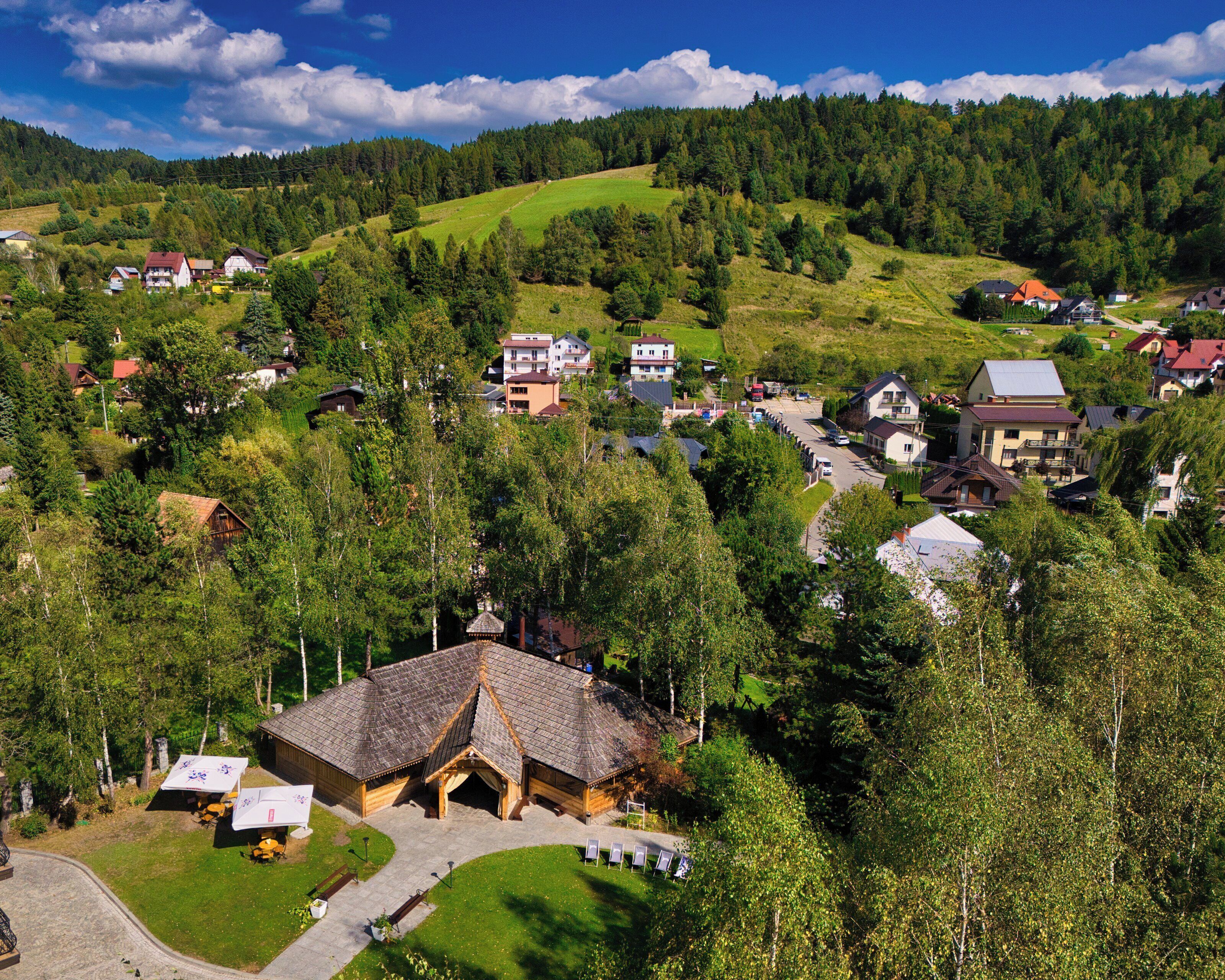 Ein ländliches Dorf mit Häusern, ein Holzgebäude mit Ziegeldach und ein bewaldeter Hügel im Hintergrund.