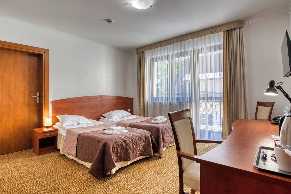 Una camera d'albergo con due letti, una scrivania, una sedia, una lampada e vista all'esterno dalla finestra.
