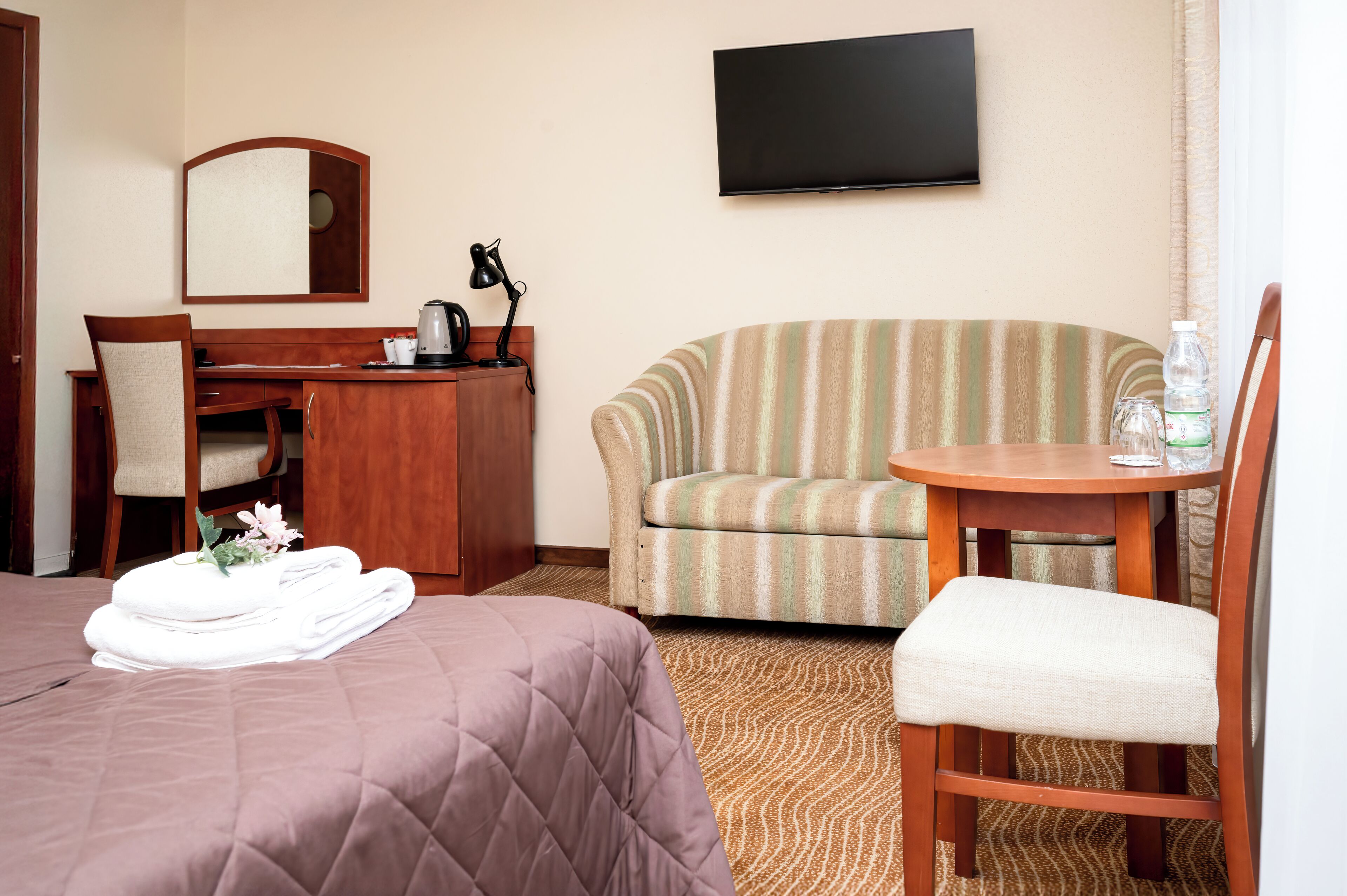 A hotel room with a bed, a desk, a chair, a sofa, and a TV.