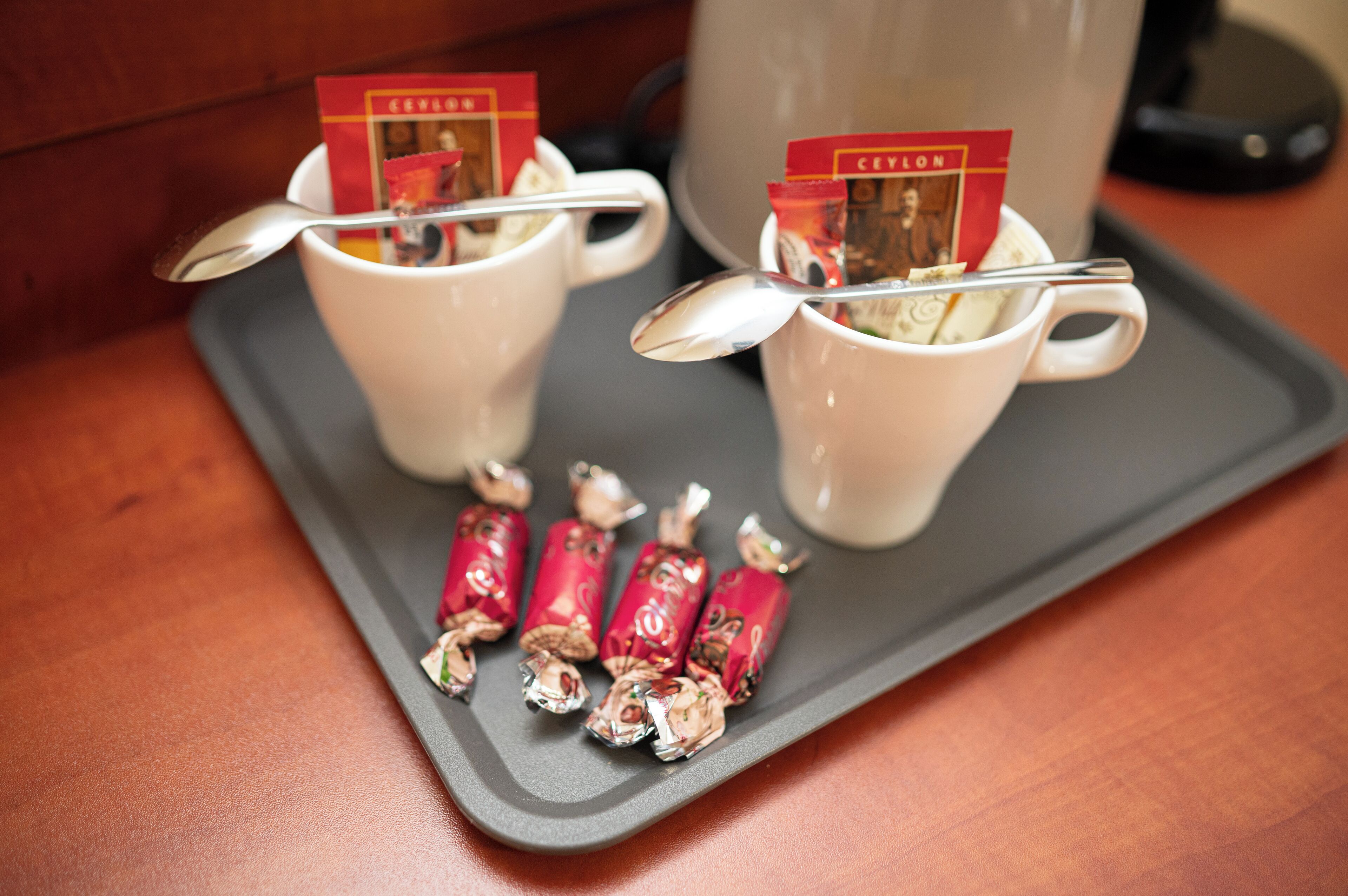Two white cups with spoons, each containing a tea packet, on a tray with wrapped candies.