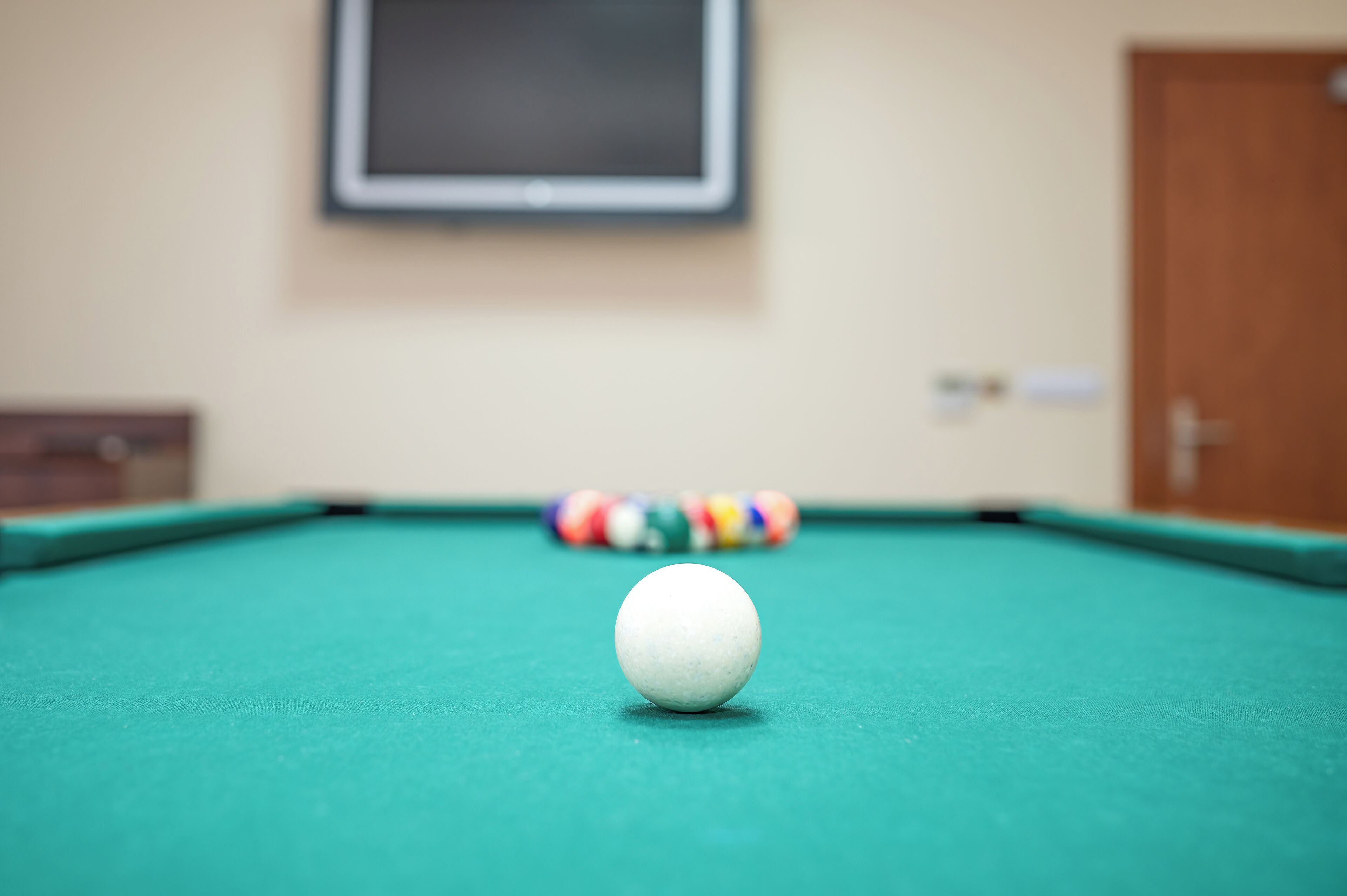 A pool table with a white cue ball in the foreground and a colorful striped ball in the background.