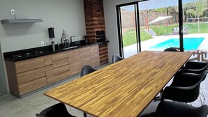 A modern kitchen with a large wooden table and black chairs, a brick fireplace, and a view of a swimming pool. - Modern house in Serra do Cipó, a peaceful place in an excellent location. (Serra do Cipó)