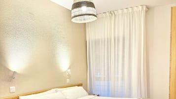 Ein Hotelzimmer mit einem großen Bett, einem Nachttisch mit einem Weinglas, einer Lampe und einem Fenster mit Vorhängen.