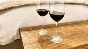 A hotel room with a bed, two wine glasses on a wooden table, and a nightstand. - HS Altet Suites - Alicante Airport (Elche)