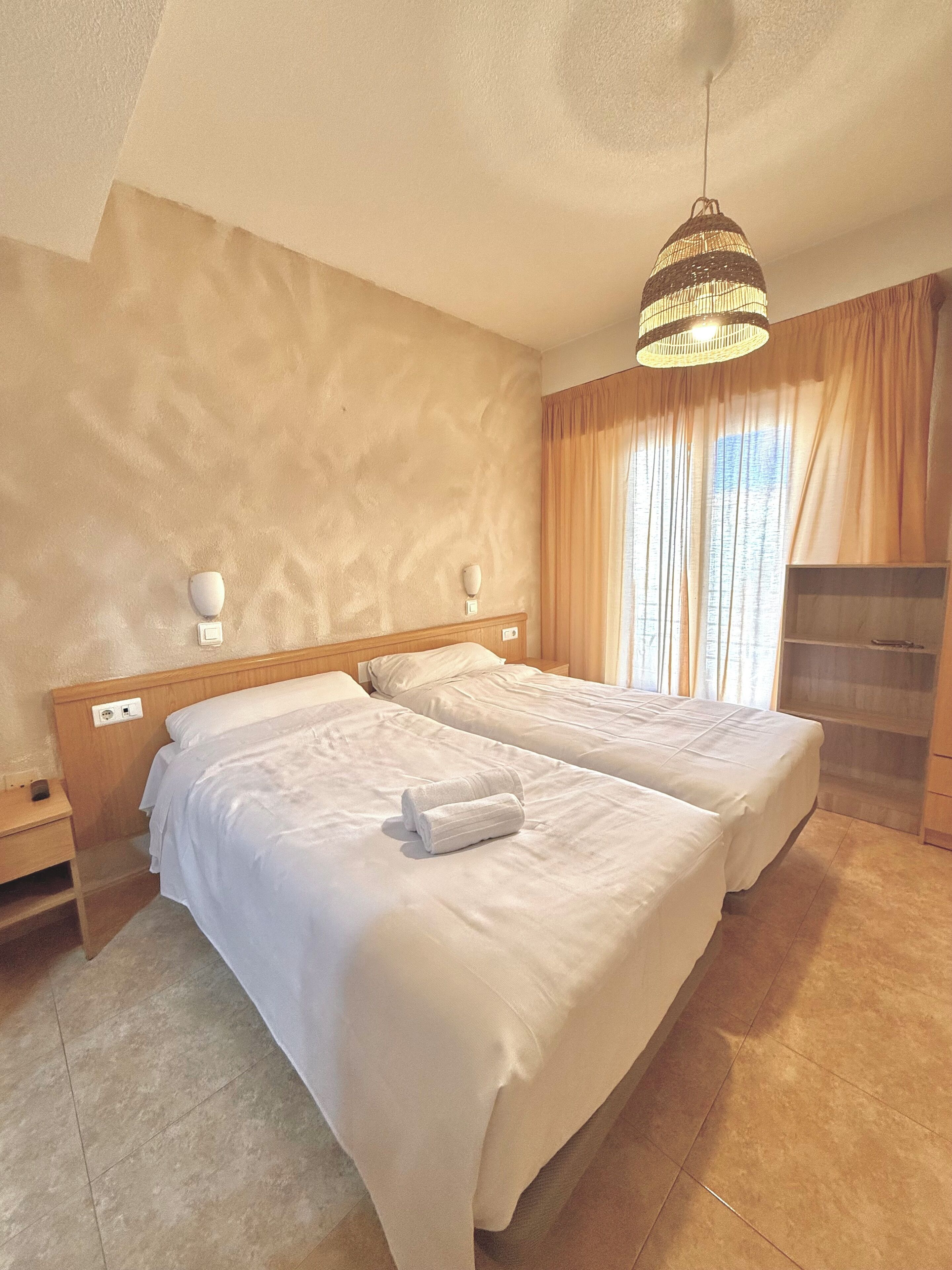 Ein Hotelzimmer mit zwei Betten, einem hölzernen Kopfteil, einer Pendelleuchte und einem eingebauten Kleiderschrank.