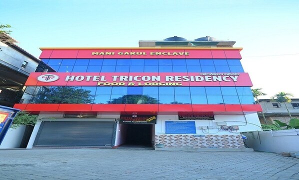 A hotel named "Hotel Tricon Residency" with a red and blue facade, featuring a prominent logo and signage for "Mami Gakul Enclave." - Hotel Tricon Residency (Guwahati)