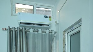 A small room with a window, an air conditioner, a curtain, a door, and a tiled floor. - Hotel Tricon Residency (Guwahati)
