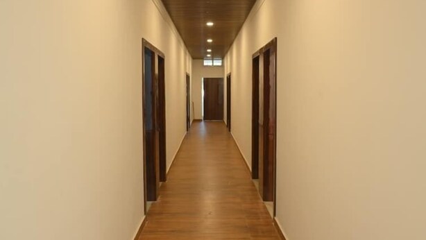 A long, narrow hallway with wooden flooring and white walls, leading to multiple doors. - Hotel Tricon Residency (Guwahati)