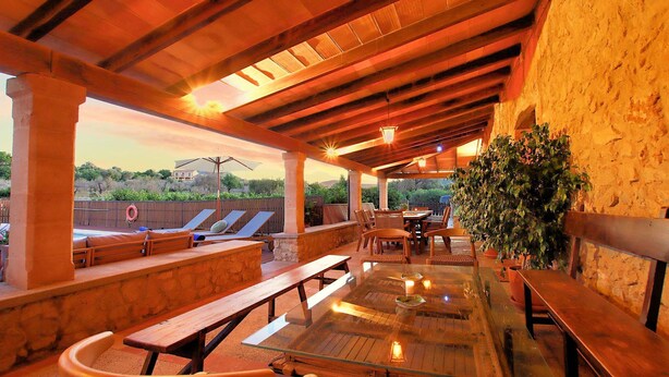 An outdoor patio with wooden benches, a glass table, and potted plants. - Finca Casou | Pollensa | Spacious countryside retreat with pool for. (Pollensa)