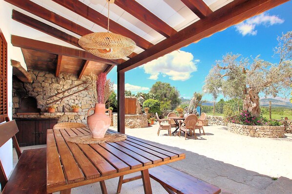 Une terrasse extérieure avec une table et des chaises en bois, une cheminée en pierre et une vue sur le paysage environnant.