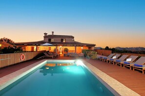 A poolside area with lounge chairs, a lifebuoy, and a house with a tiled roof. - Finca Casou | Pollensa | Spacious countryside retreat with pool for. (Pollensa)