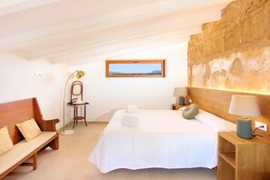 Une chambre à coucher avec un grand lit, un banc en bois, un bureau, une lampe et un tableau encadré au mur.